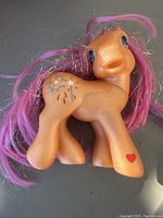 Photo showing front and side view of the orange Sparkleworks II pony with glitter, purple and pink hair, and colorful cutie mark on flank.