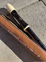 Black plastic soprano recorder with cream-colored mouthpiece and rings placed beside a brown zipper carrying case with 'Recorder Soprano ASRB-211' text.
