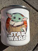 Side view of white ceramic Star Wars Baby Yoda mug with metal rim showing the character Grogu and Star Wars logo on an orange background.