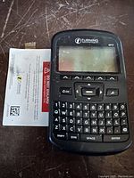 Top-front view of the Turning Technologies QT2 clicker showing the screen, navigation buttons, and keyboard, alongside a user guide.