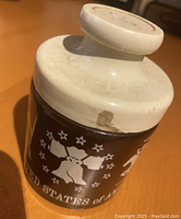 Top side view showing the white screw-off lid with visible minor stains and marks, upper section of brown glass jar with white printed map of the United States and stars.