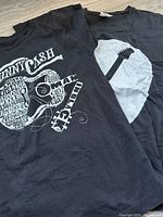 Set showing two black women's t-shirts with guitar-related white graphic designs, one featuring Johnny Cash text and an intricate guitar shape, the other a simple electric guitar silhouette.