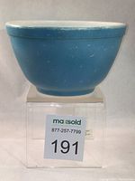 Side view of vintage blue Pyrex mixing bowl showing surface scratches and paint loss on blue exterior and white interior.
