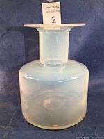 Front view of the opalescent glass vase showing the smooth cylindrical shape with wide flared rim against a blue backdrop.