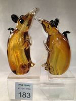Front view of two amber glass rat figurines highlighting gold silver foil inside and black glass ears and tail.