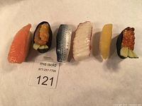 Top down photo showing all 6 artificial sushi pieces in a row including salmon, uni gunkan, silver fish, white fish, yellow nigiri, and ikura gunkan sushi.