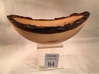 Side profile of oval-shaped wooden bowl showing live bark edge and smooth interior surface with amber maple wood tones.