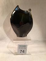 Front view of the black oval ceramic vase sitting on a clear stand with lot number 74.