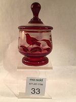 Front view of ruby glass lidded vase showing bird and plant design in red and gold accents