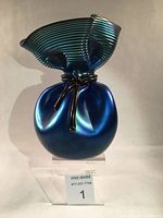 Front view of iridescent teal and purple aurene art glass vase shaped like a tied bag with ribbed flared top.
