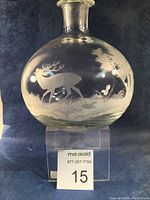 Front view of round glass wine decanter with etched stag and forest scene