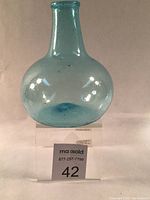 Front view of aquamarine glass bottle showing globular onion-shaped body and medium tapered neck with applied rounded mouth.