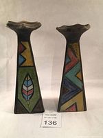 Front view of two Raku pottery candlesticks/vases with multicolored mosaic geometric patterns and feather motif on the left piece.