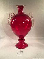 Front view of large ruby red blown glass vase with clear glass handles, showing shape and color.