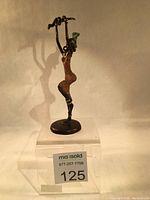 Full view of the bronze sculpture showing woman in dress holding child above head, positioned on a black round base.