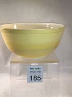 Front side view of yellow Pyrex bowl displaying shape, size and wear on exterior surface.