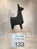 Front left angled portrait of black ridged cast iron llama or alpaca sculpture on display stand with lot number.