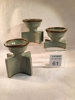 Three stoneware candlesticks of different sizes with celadon glaze and mottled iron glaze on rims, shown on clear stands with a sales tag.