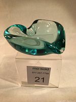 Front angled view of heart shaped turquoise green blown glass dish on clear riser base.
