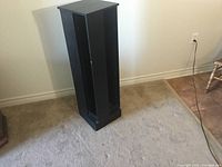 CD tower photographed standing on carpeted floor near a wall with electrical outlets, showing front and side views.
