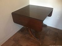 Photo showing one side of the hardwood dining table with drop ends and pedestal base with four curved legs.