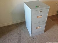 Front and angled view of gray steel 2 drawer filing cabinet with keys on top