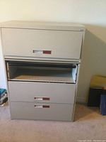 Steel 4 drawer filing cabinet with a beige/light gray color, one drawer is open showing interior with measuring scale.