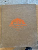 Brown hardcover book front with embossed title in orange, showing some wear at edges.