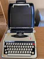 Open typewriter showing cream-colored body, detailed keyboard with white keys, black letters and numbers, and red functional keys.
