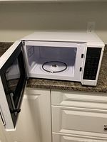 White Midea microwave oven with door open showing interior glass turntable and white interior.