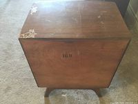 Side view of wooden night table with peeling finish visible on top corners, overall condition visible.