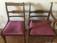 Two wooden chairs side by side against a wall. One chair includes armrests, the other does not. Both have red fabric seats. One chair has an armrest detached and resting on the seat.