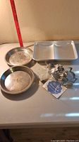 Two round pie tins, one aluminum book-shaped cake pan, several Ann Clark cookie cutters laid out on a white table with a measuring tape for scale.