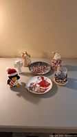 Full view of all Christmas items including two round Santa plates, realistic Santa figurine, mini hurricane holder with Christmas base, white angel figurine and ornament, and penguin plush toy.