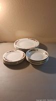 Three stacks of white china plates with floral and ribbon decoration: 4 salad, 4 bread, and 4 dinner plates