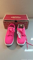 Front view of bright pink Vans shoes with original box in background.