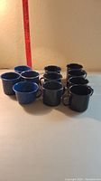Front-side view of all 11 blue and black metal camping mugs arranged in rows.