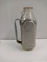 Front view of vintage 1950s milk jug showing clear glass top and textured aluminum body and handle.