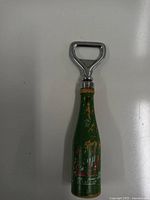 Full view of the 7 Up bottle shaped bottle opener standing upright, showing metal opener top and green bottle body with paint chips.