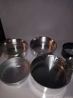 Five aluminum circular cake pans on white background. Three pans have waffle textured bases, others have smooth surfaces. Pans appear clean and lightly used.