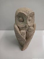 Front angle view of the owl family statue, showing the large owl with two smaller owls nestled in its wings. The texture and carved feather details are visible.