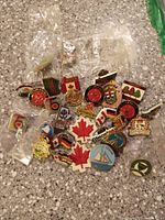 Wide view of various collectible Canadian pins on a surface including multiple maple leaf pins and city/prvince related pins.