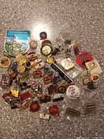 Overhead photo showing a mixed collection of enamel collectible pins on a gray speckled surface.