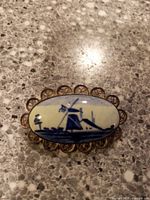 Front view of the brooch showing detailed Delft blue windmill painting on oval ceramic set in filigree frame