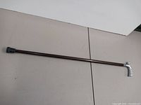 Full length view showing cane's dark shaft and silver pistol grip handle with rubber tip at base.