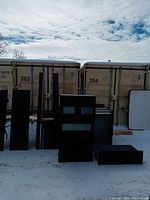 Dismantled bedroom furniture parts placed outdoors showing dresser, side tables, drawers, bed frame components, and mattress leaning against container.
