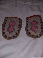 Two matching pairs of hand-beaded indigenous moccasin patches lying adjacent on a fabric surface, showing symmetrical beadwork and leather edges.