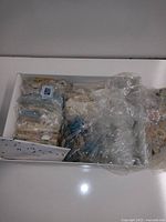 Top view of a white cardboard box filled with multiple plastic bags containing assorted postage stamps.