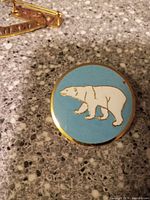 Front view of circular badge showing white polar bear on light blue background with gold edging