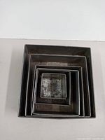 Photo of five nested square metal cake tins showing varying sizes and surface wear.